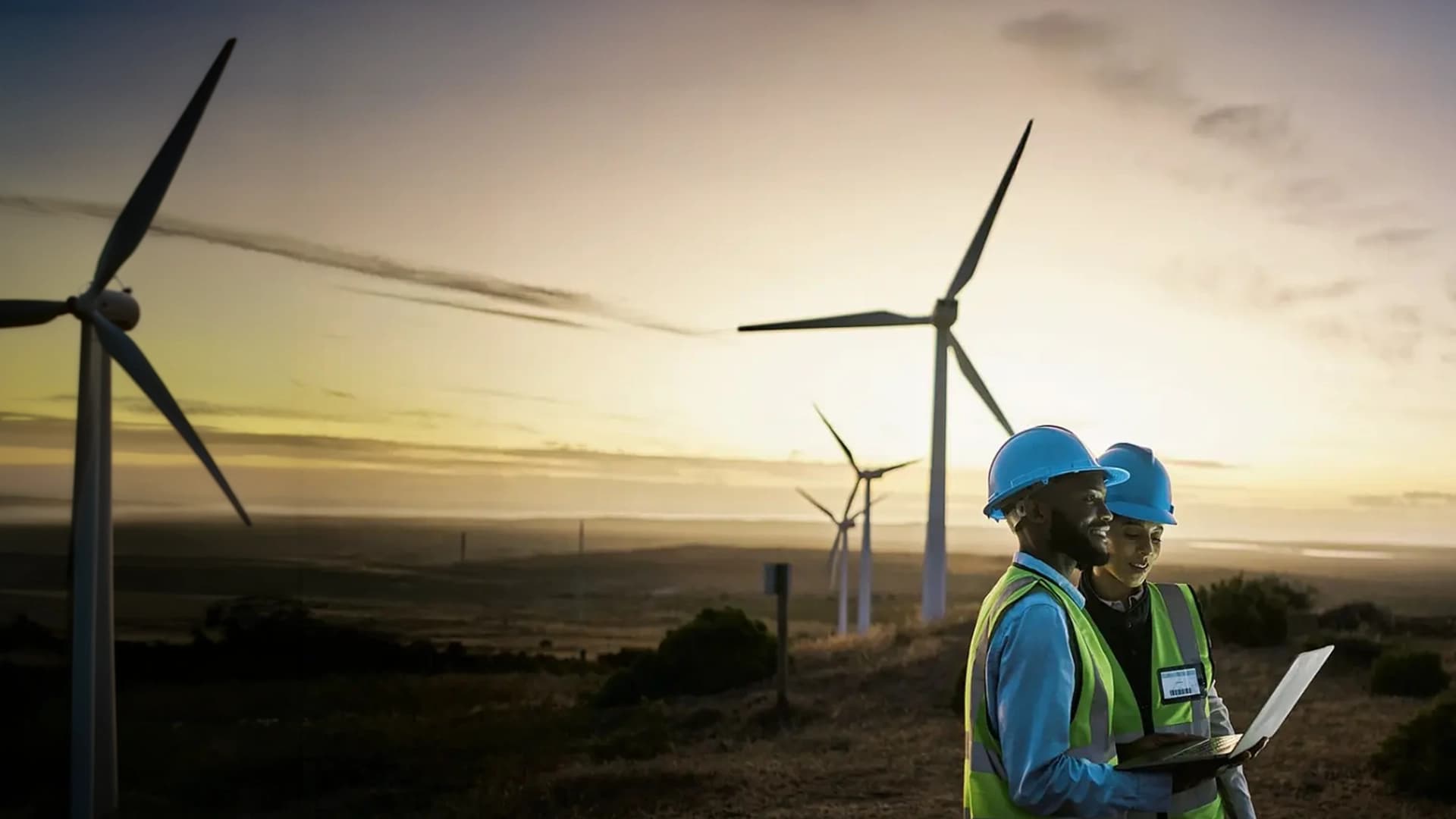 Two environmental workers in a field with wind turbines