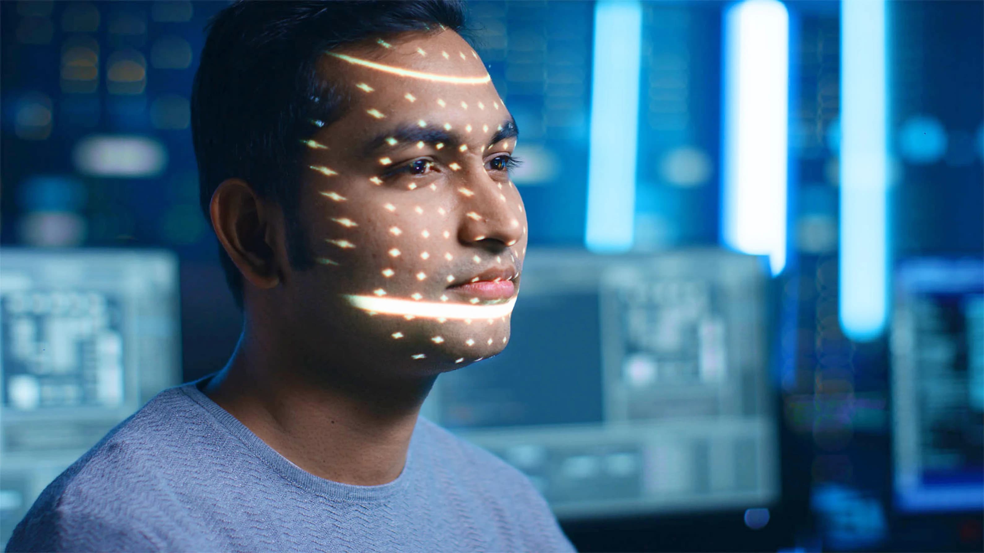 Person working in front of multiple computer screens in a blue-lit technology environment.
