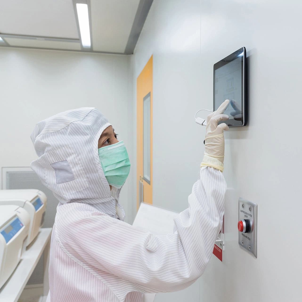 A woman in a white coat and mask interacts with a monitor, focused on the screen's content.