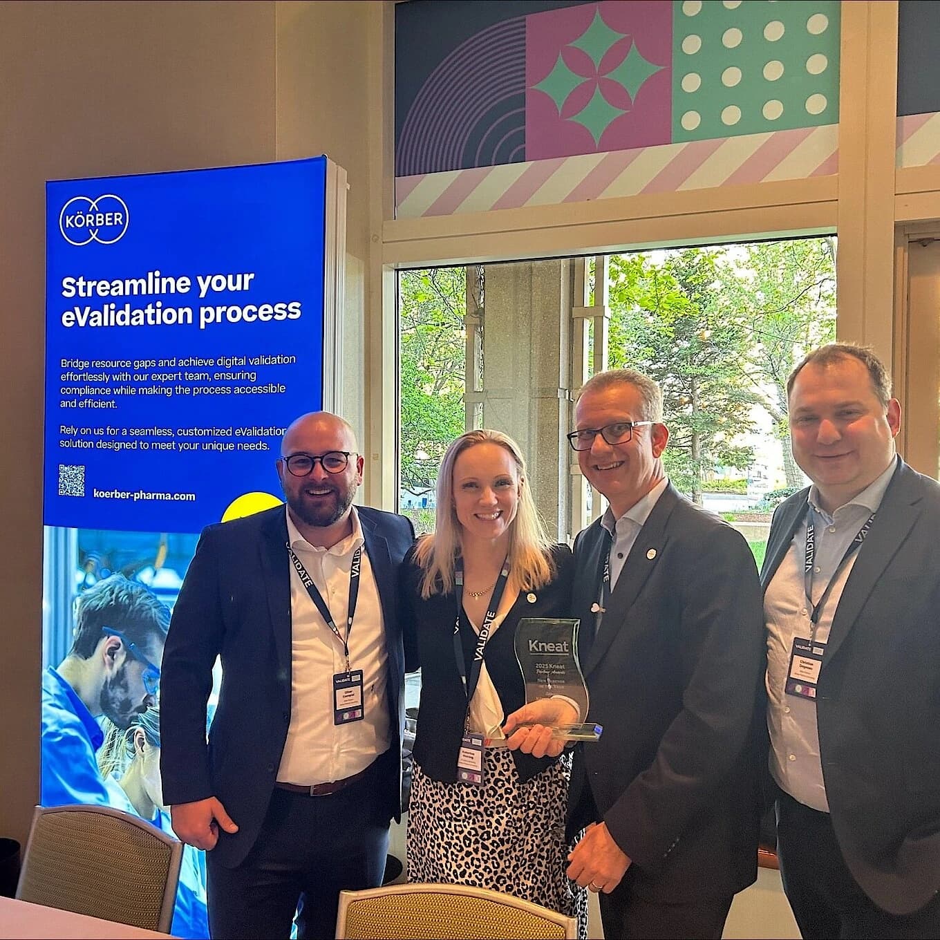 Körber team members standing together at the Validate 2025 event in Boston, holding the “Partner of the Year” award beside a Körber eValidation display.