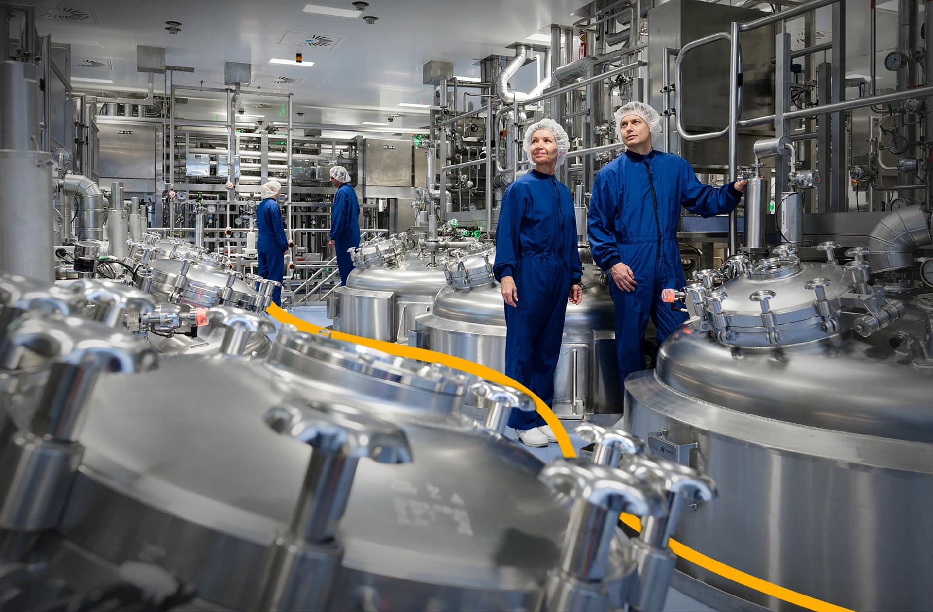 Two employees in blue overalls standing side by side in a factory setting, surrounded by machinery and equipment.