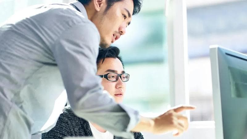 Zwei Männer blicken auf einen Computerbildschirm.