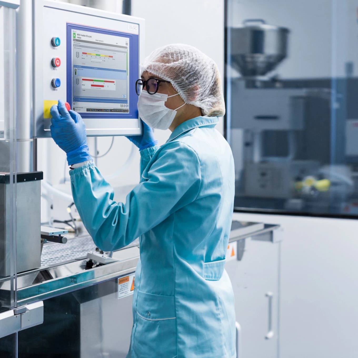 A woman in a lab coat and gloves operates a machine in a factory setting.