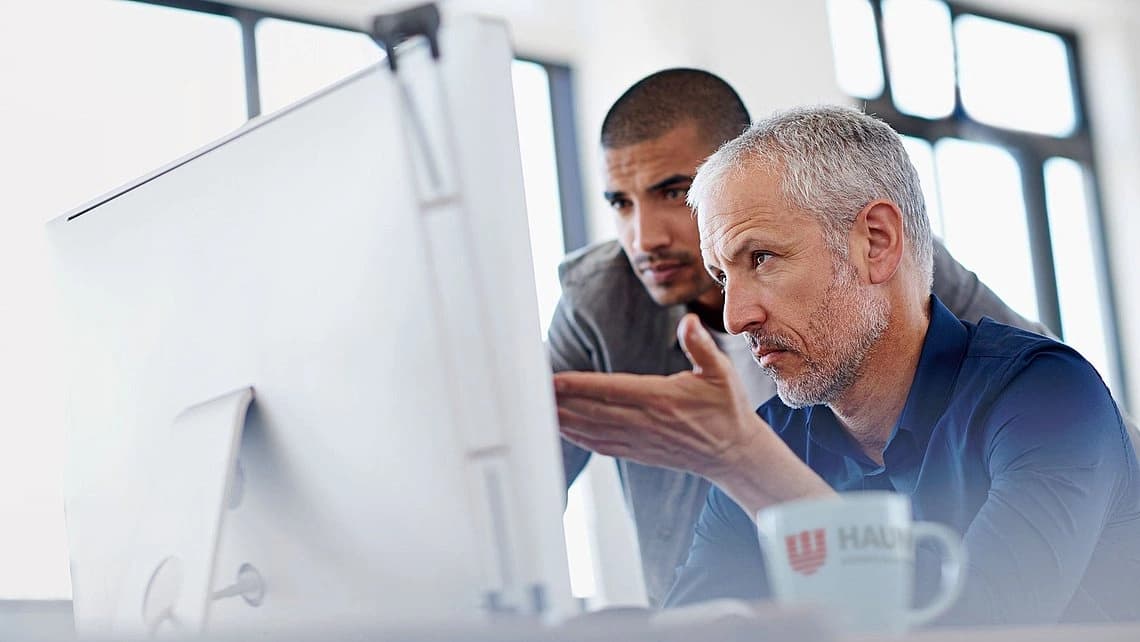 Two men focused on a computer screen, likely collaborating or reviewing information together.