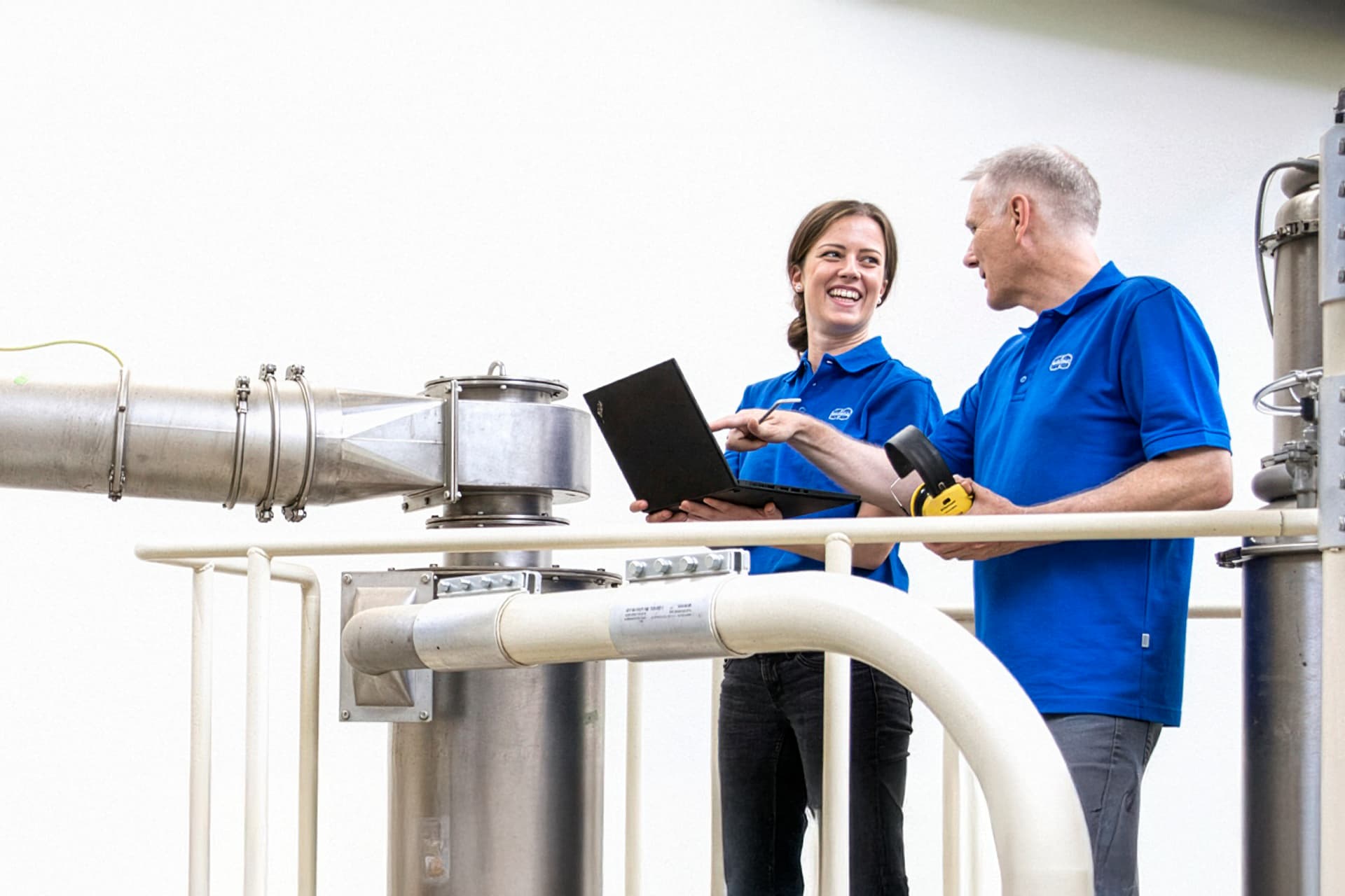 Two Körber employees stand next to a tobacco processing pipe
