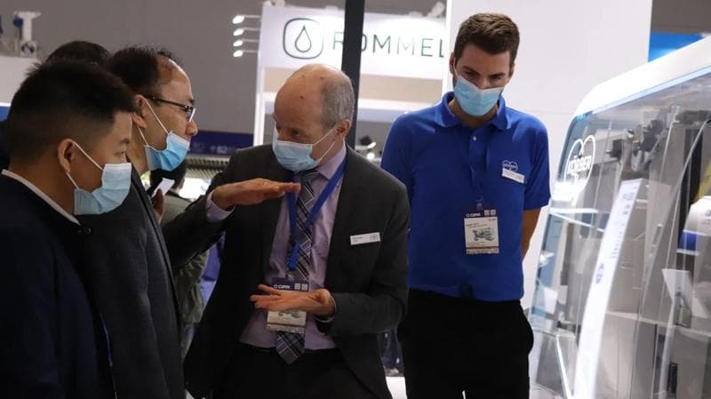 Gruppe von Menschen mit Masken, die sich neben einer Körber Pharma-Maschine unterhalten.