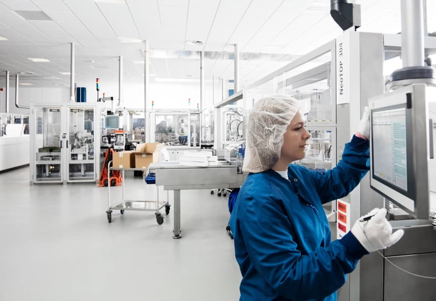 A woman works on a computer in a factory, focusing on cloud-native manufacturing in the pharma industry.