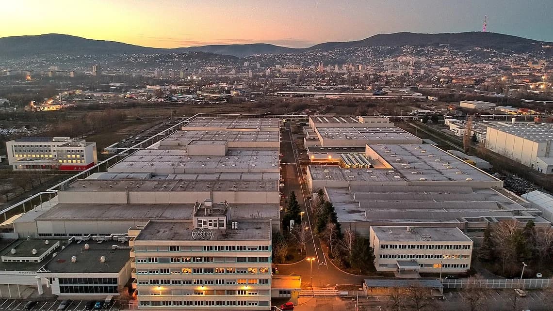 Sunset aerial view of Körber’s Pécs campus in Hungary, highlighting the manufacturing buildings with the city and hills in the background.