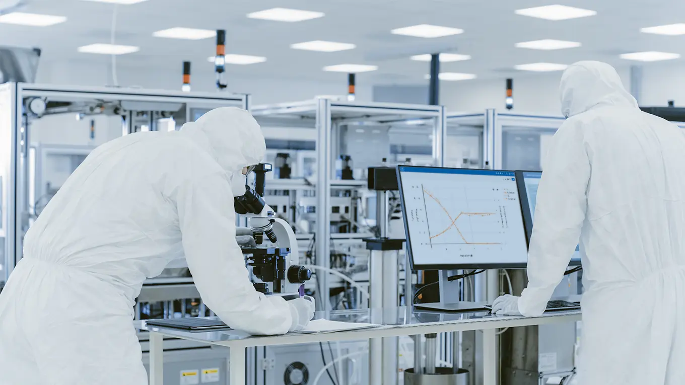 Two people in white suits collaborate on a computer for bioprocess development in the pharmaceutical industry