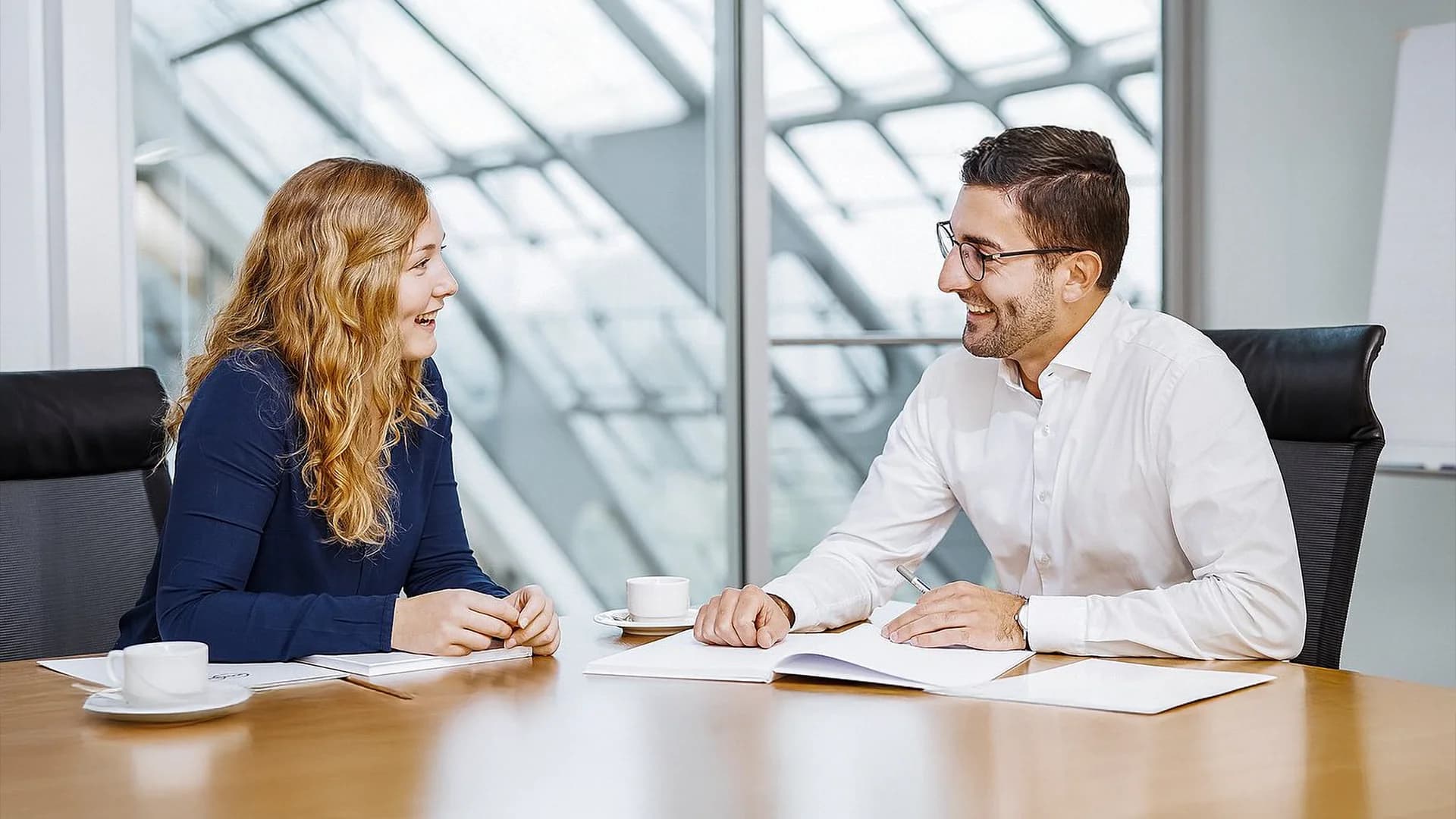Ein Mann und eine Frau sitzen an einem Tisch in einem Büro und diskutieren über arbeitsbezogene Themen.