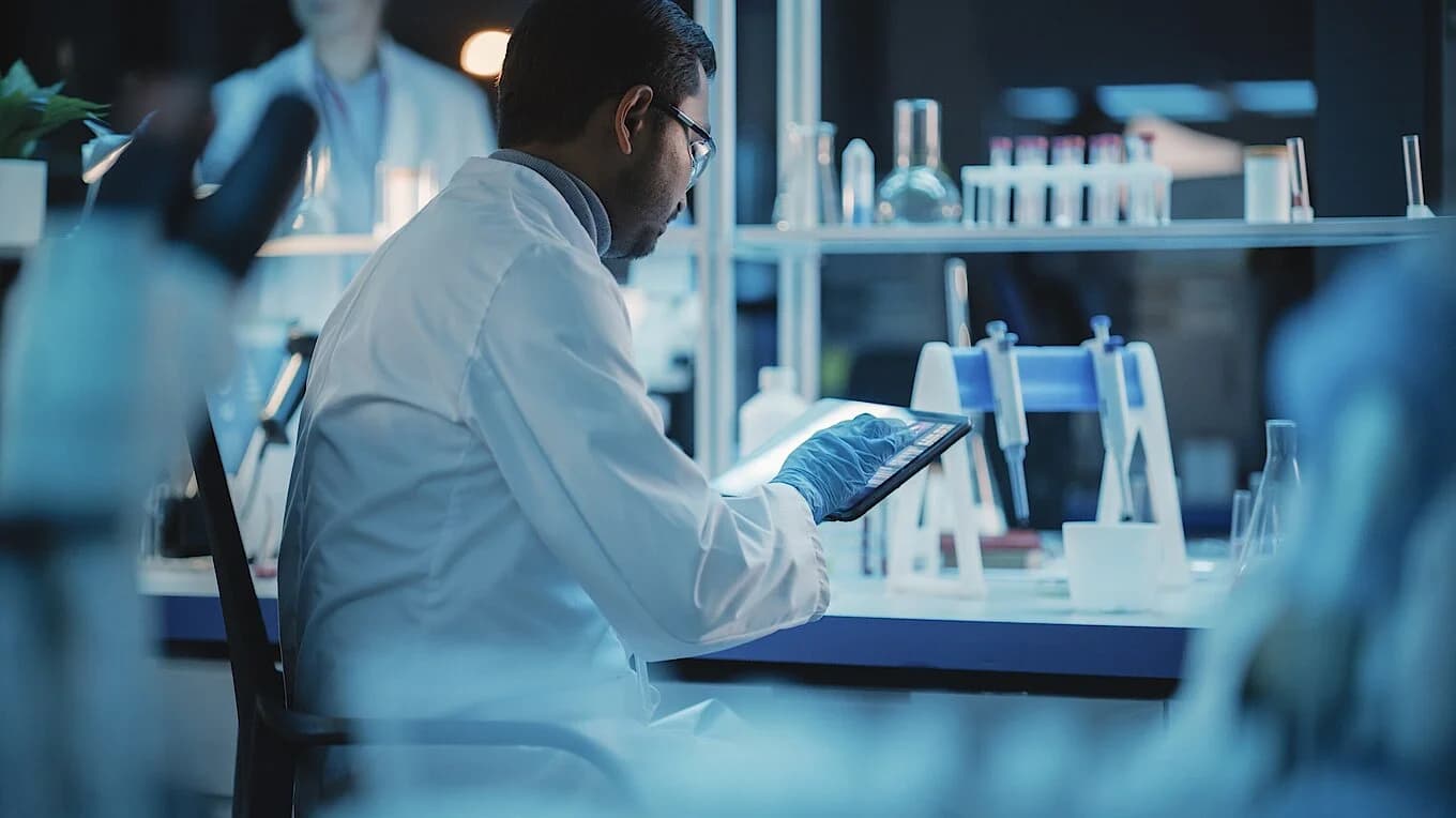 A man in a lab coat is focused on working with a tablet in a laboratory setting.