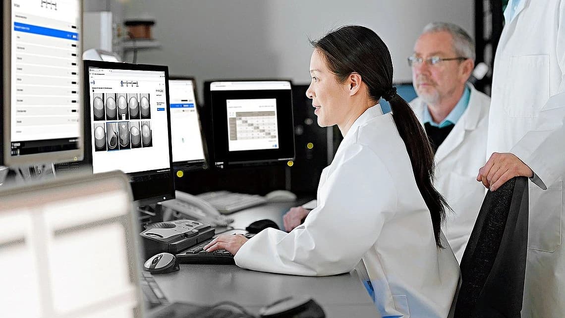 Ein Mann und eine Frau in Laborkitteln arbeiten an Computern für die KI-gestützte pharmazeutische Inspektion.
