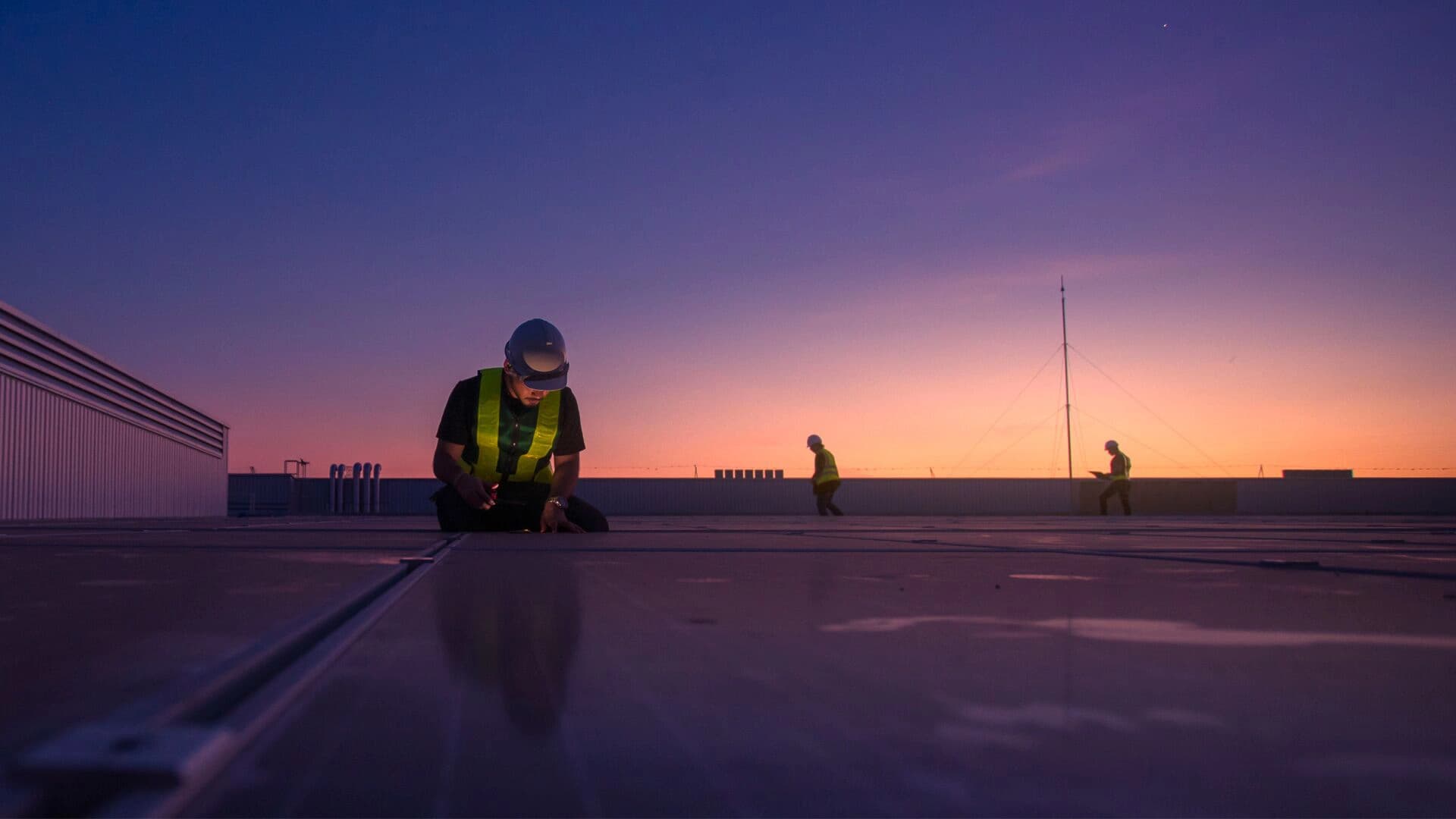 Silhouetted workers on a rooftop during a vibrant sunset.