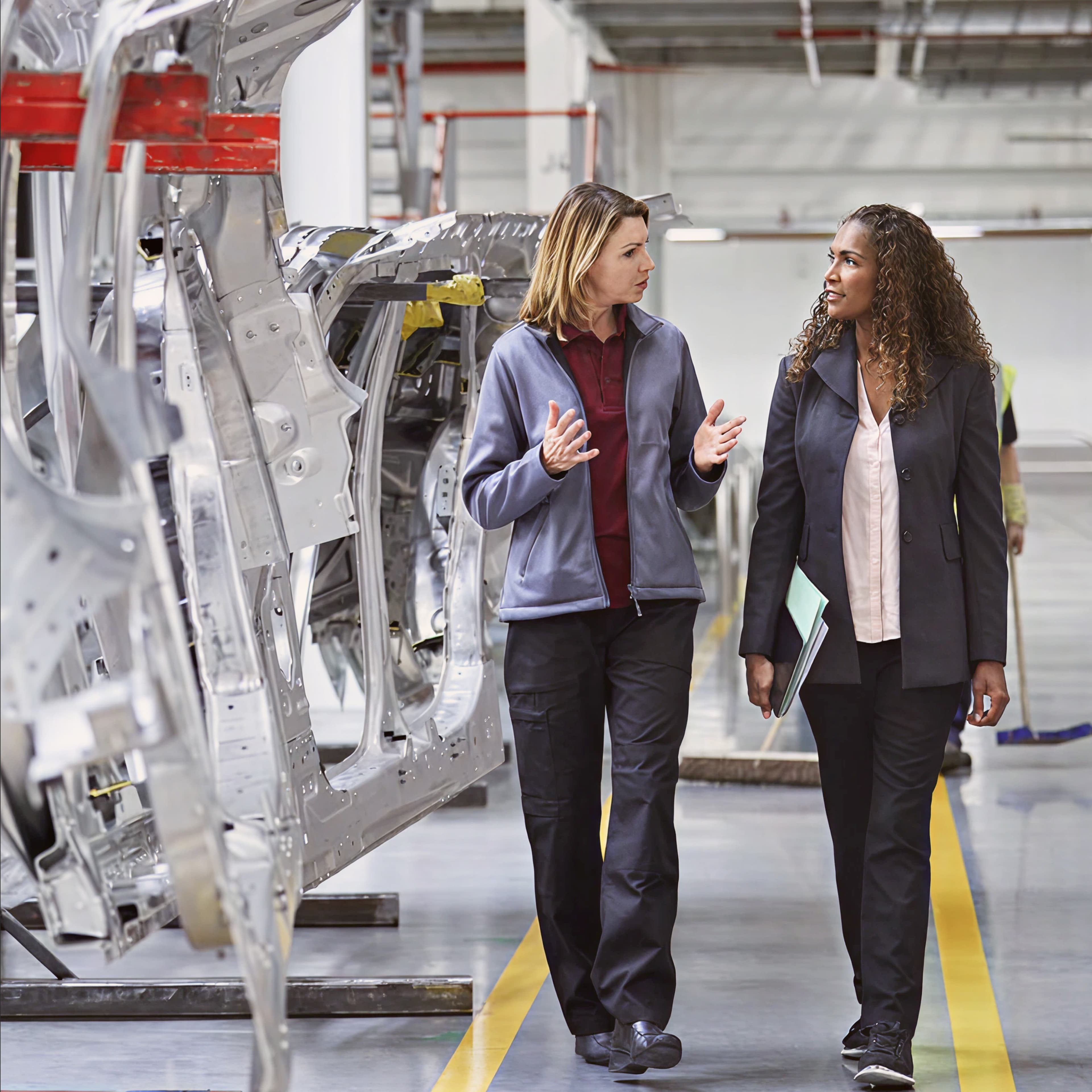 Two woman talking in a car parts factory