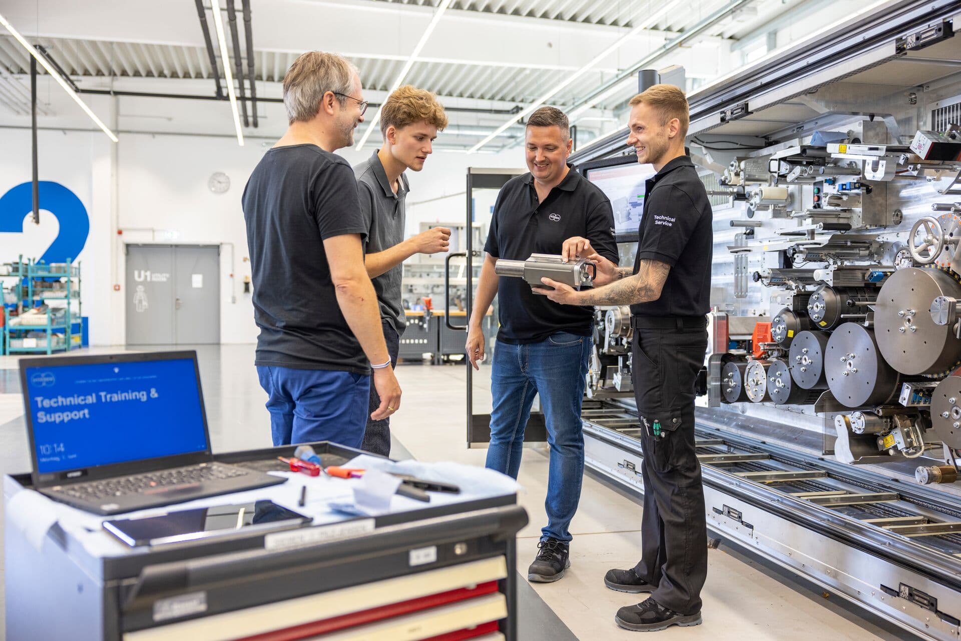 Three factory workers gathered around a laptop, discussing content from the Körber Academy platform.