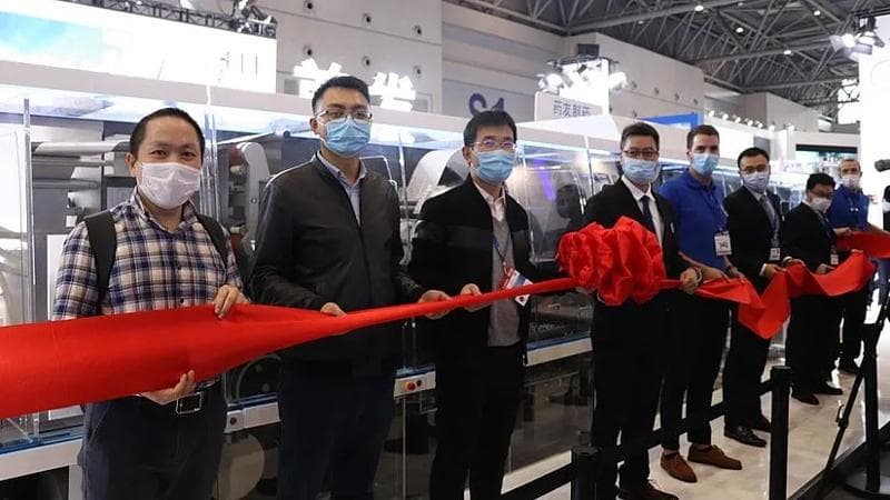 Gruppe von Menschen mit Masken, die ein rotes Band halten.