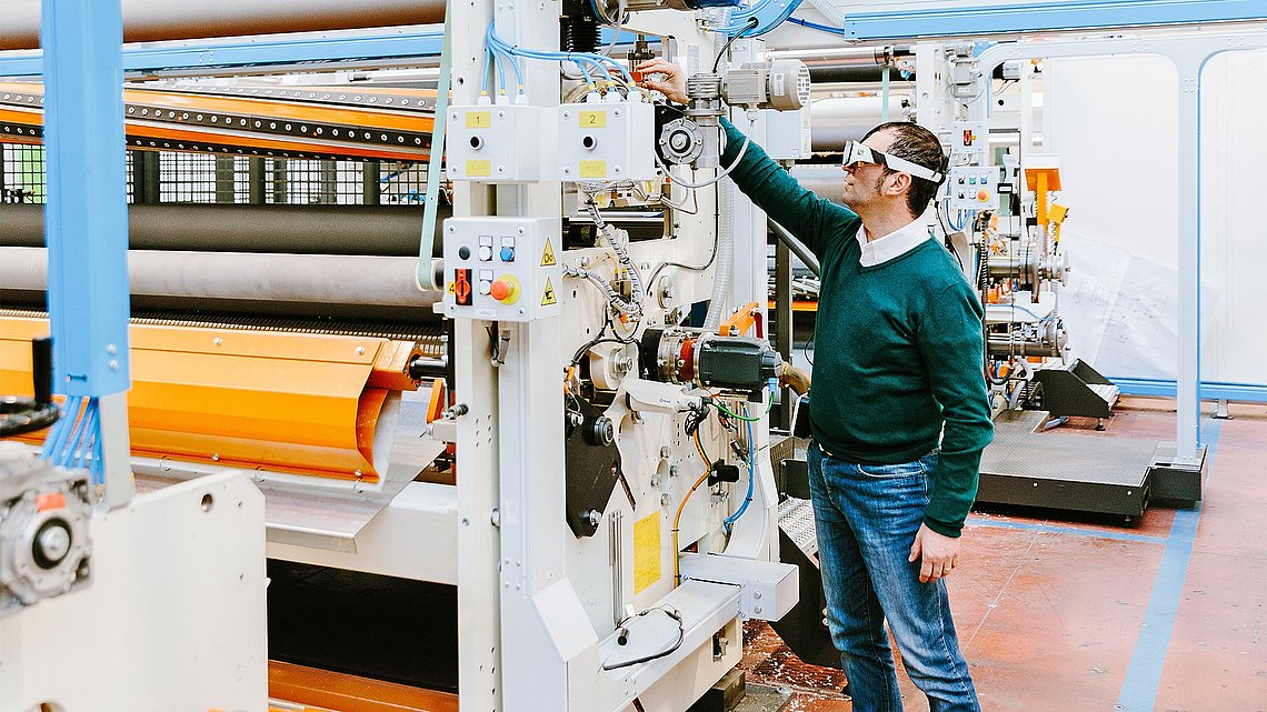 Foto eines Servicetechniker, der mit einer Augmented-Reality-Brille auf dem Kopf eine Maschine wartet